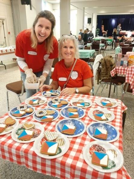 Women smiling women in red shirts at a table with plates of cookies

Description automatically generated